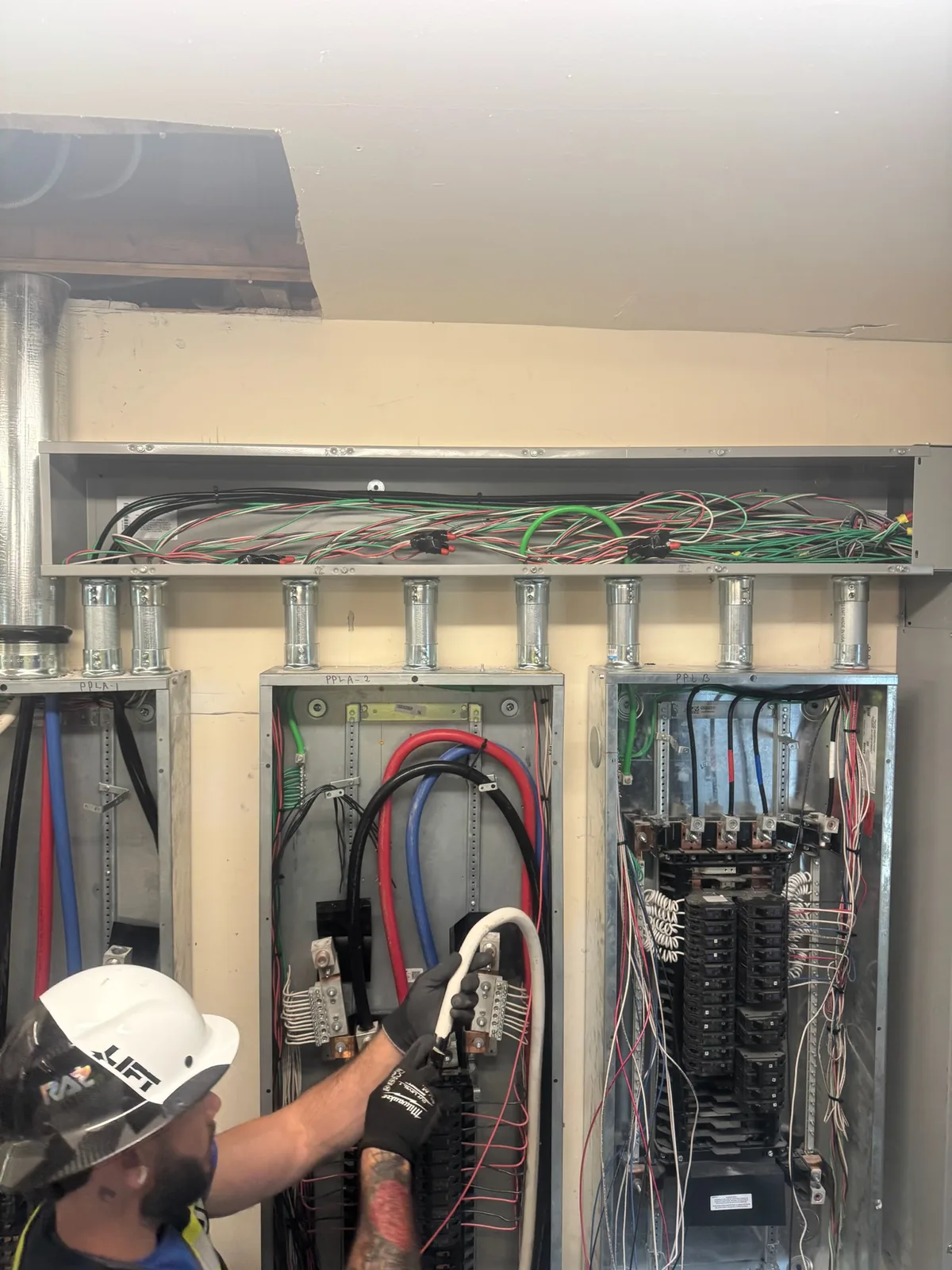 Electrician in a hard hat landing feeder conductors in a commercial panel